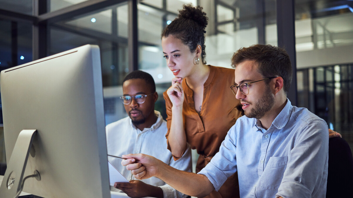 Three technical specialists discussing work at a shared computer.