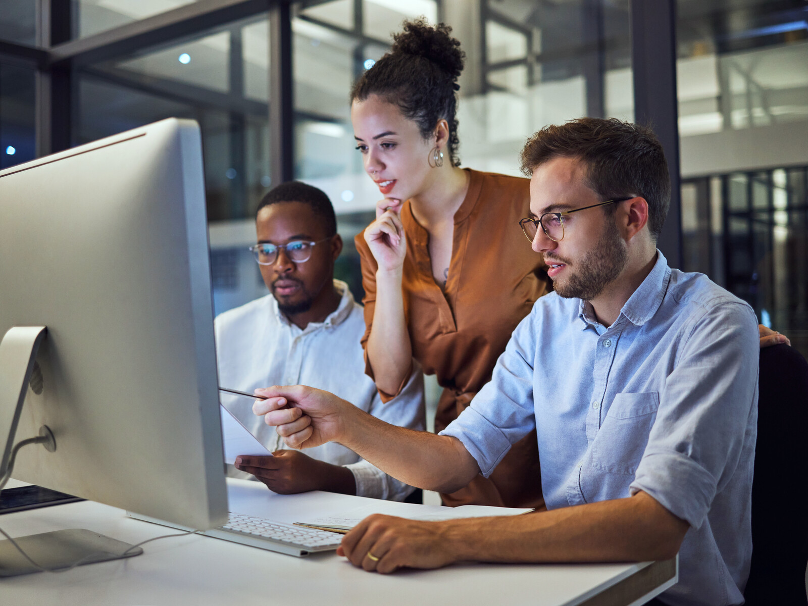 Three technical specialists discussing work at a shared computer.